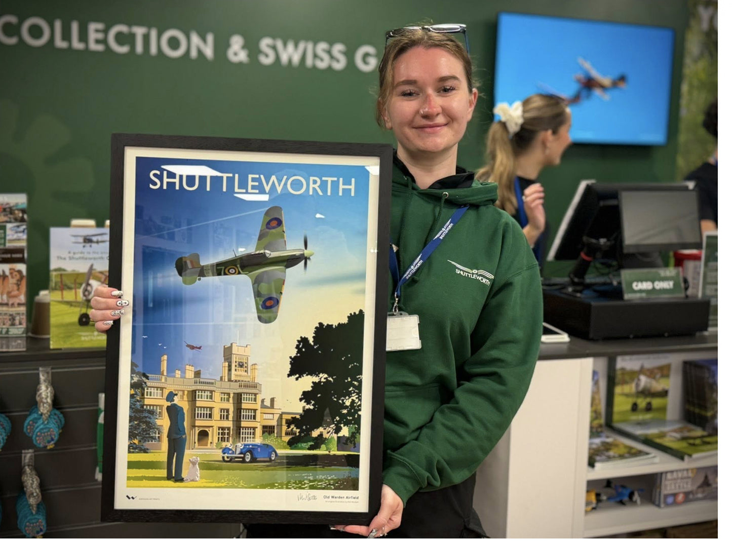 Young woman holding a framed poster of Shuttleworth Collection in the Shuttleworth Collection's gift shop.