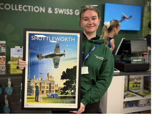 Young woman holding a framed poster of Shuttleworth Collection in the Shuttleworth Collection's gift shop.